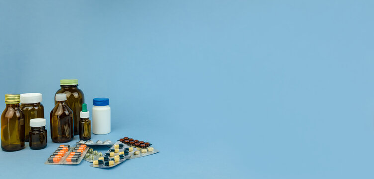Assortment of pharmaceutical tablets and capsules in blister packs alongside medicine bottles arranged on a blue background. The commercial medical still life represents medication, pharmacy