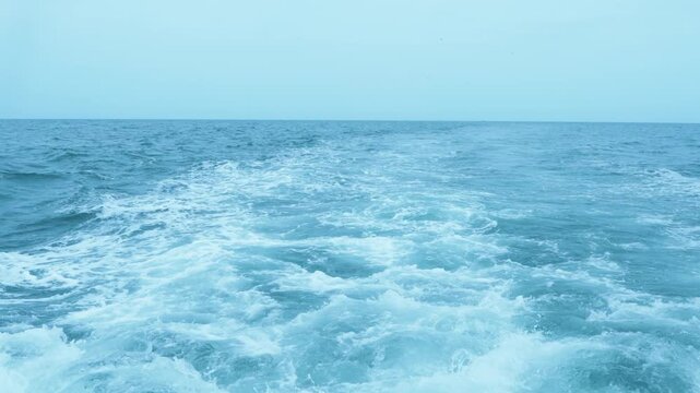 White foamy wake left by a boat on the turquoise blue ocean surface under a clear sky. Wide seascape featuring bubbles, splashes, and ripples in the water. Beautiful maritime background with horizon.