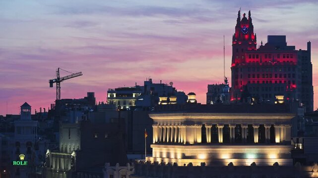 Elevated twilight perspective of Madrid skyline with Bank of Spain and red-lit Edificio Telef&oacute;nica silhouette framed against a pink sunset sky, urban architecture b-roll.