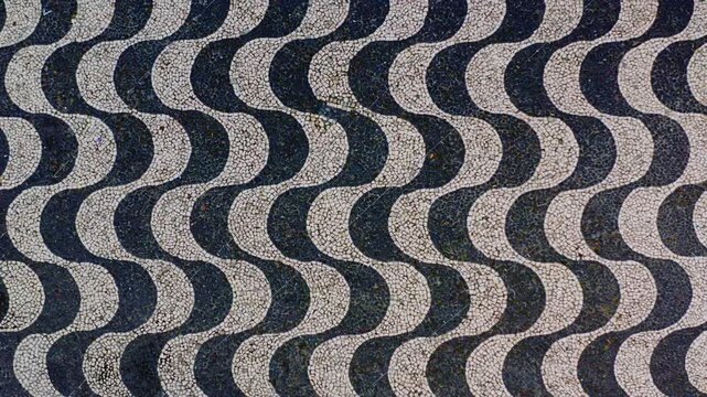 Top down aerial drone flight over the black and white wave cobblestone mosaic of Largo de Sao Sebastiao plaza, Portuguese pavement pattern filling the frame, abstract graphic texture, Manaus, Brazil.