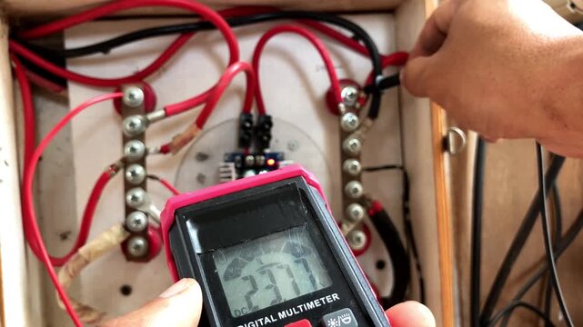Close-up of a technician's hands using a digital multimeter to test voltage on electrical wiring and components inside a solar power panel control box.