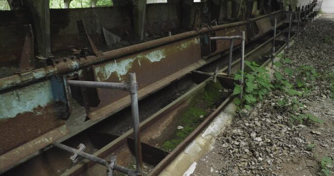 Camera pans along rusted metal feeding troughs inside a derelict barn.