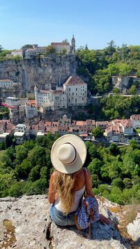 woman tourist in hat sitting on cliff enjoying rocamadour medieval village view france