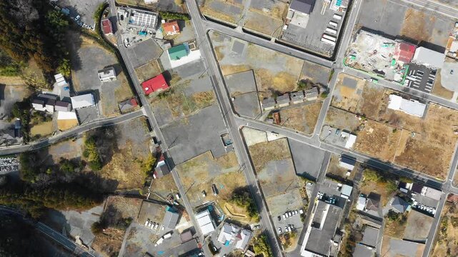 A top-down aerial view of streets, vacant lots, and buildings in Tomioka, Japan.