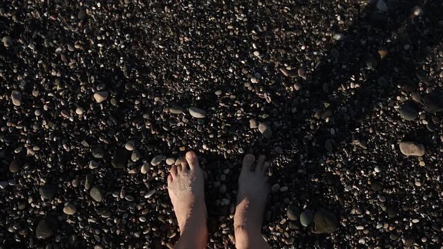 Close-up of bare feet on dark pebbles, textured shoreline, intimate beach moment, tactile coastal scene.