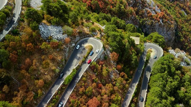Lovcen Serpentine Montenegro features cars on twisting mountain road cut into rugged slopes. Serpentine route threads through vivid autumn trees, creating calm yet striking travel landscape.