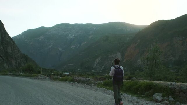 A female traveler with a backpack walks along a path, with the immense mountains of the Peruvian Andes in the background.