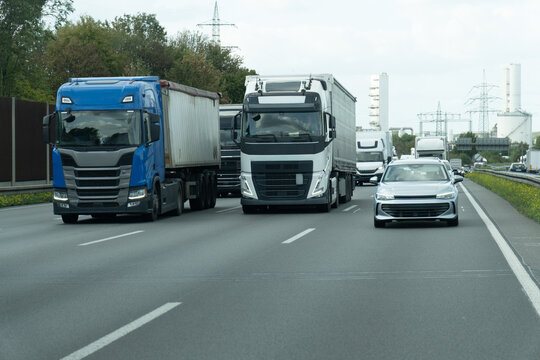 Freight trucks and passenger car traveling on busy highway near industrial infrastructure