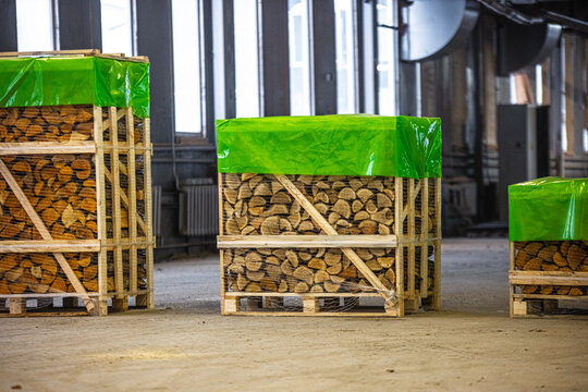 View of stacked firewood in wooden crates covered with green plastic sheets inside a warehouse in Latvia.