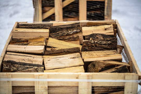 View of a wooden crate filled with neatly stacked chopped firewood pieces, with snow visible in the background, Latvia.