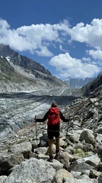 hiker with red backpack looking at alpine glacier on rocky mountain trail