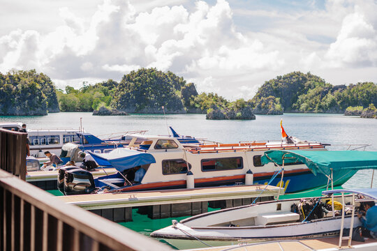View of boats docked at a pier in a tropical bay with karst islands in the background, Raja Ampat, Southwest Papua, Indonesia.