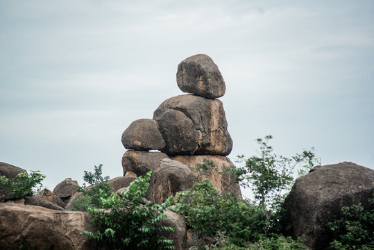 View of naturally stacked granite boulders surrounded by lush green vegetation under a cloudy sky in Jos North, Plateau, Nigeria.