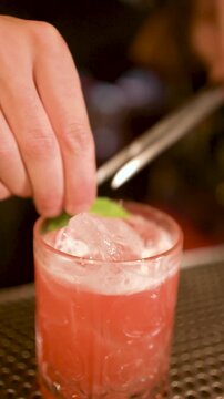 close up of barman hands finishing red cocktail in a bar at night, concept of drinking out and nightlife