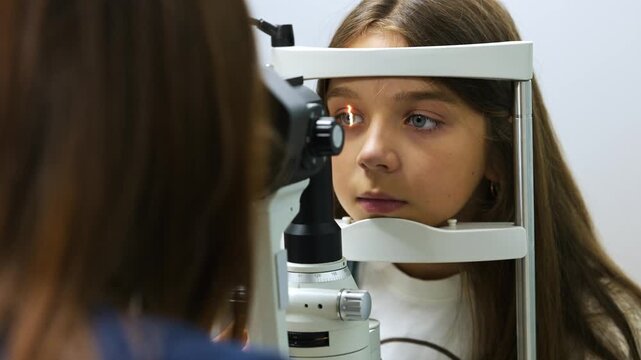 Young girl receives an eye exam from an optometrist using a phoropter in a well-equipped clinic, with various medical supplies in the background