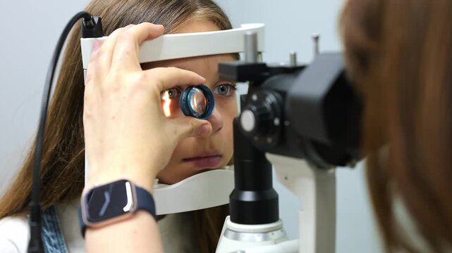 Female optometrist performs eye exam on patient with slit lamp in a modern clinic, featuring medical equipment and a computer in the background