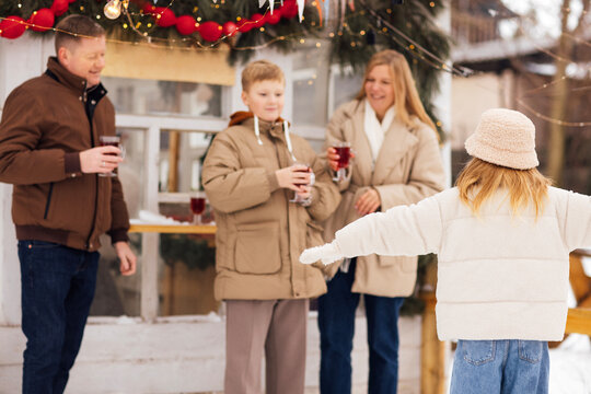 Family enjoying winter holiday drinks outdoors, dressed in warm coats, with festive decorations and a cozy atmosphere in a snowy setting