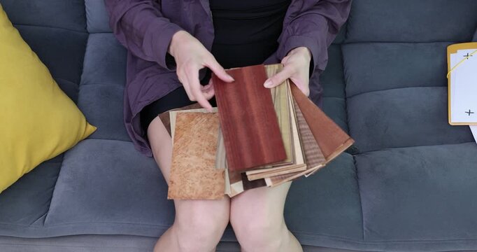Woman holds parquet board samples in different warm shades. Female sits on sofa and carefully compares colors and textures of samples. Time lapse