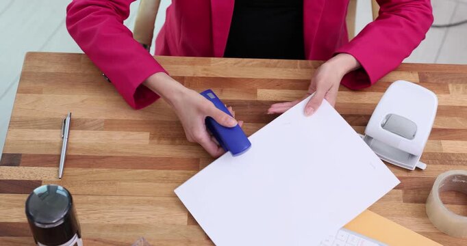 Office worker tries to repair stubborn metal stapler at table. Woman presses stapler white sheet of paper hoping to restore device. Time lapse