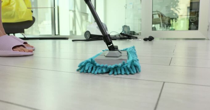 Conscientious woman cleans laminate floor with soft microfiber mop. Diligent housewife removes ordinary household dirt in spacious living room