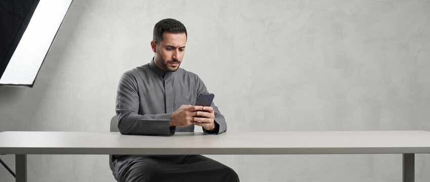 Man in grey thawb using smartphone at table