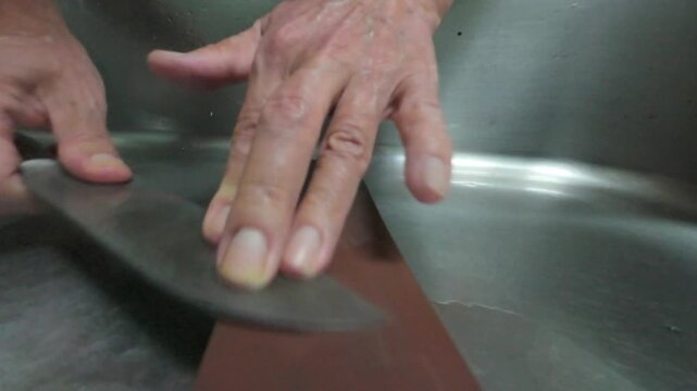 Close-up of hands sharpening the tip of a kitchen knife on a whetstone