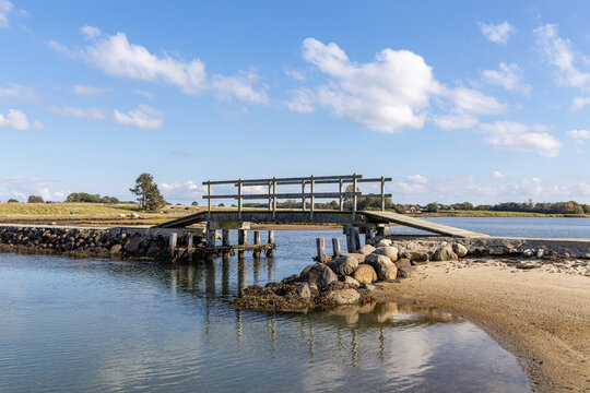 View of the wooden bridge on the island of Hjarno with a sandy shoreline and calm water under a blue sky in Hjarno, Hedensted Municipality, Denmark.