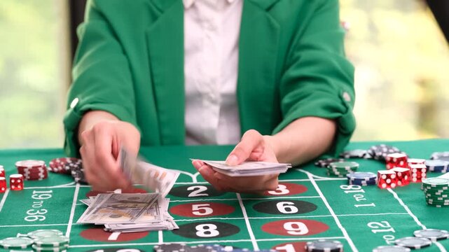 Casino dealer sits at gaming table with colorful chips and counts crisp dollar bills. Woman manages money and game equipment with attention time lapse