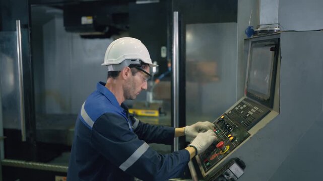 Worker monitors machine with focused attention. He wears hard hat and safety gear. Controls display shows operational parameters