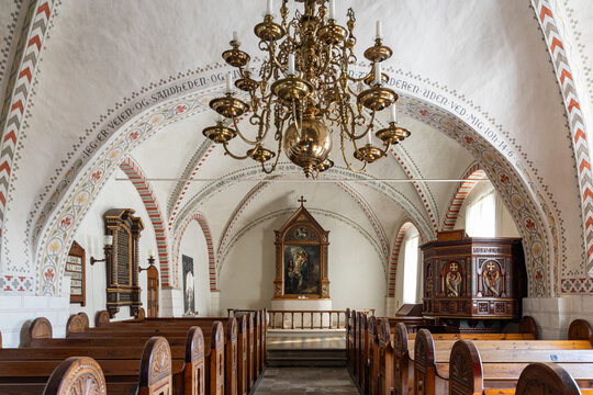 View of the historic church interior featuring a large brass chandelier, wooden pews, an ornate pulpit, and a painted altarpiece under vaulted ceilings in Kerteminde Municipality, Denmark.
