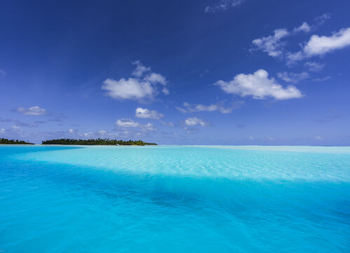 View of the turquoise lagoon surrounding One Foot Island in Aitutaki with lush palm trees and clear blue sky in Arutanga, Cook Islands.