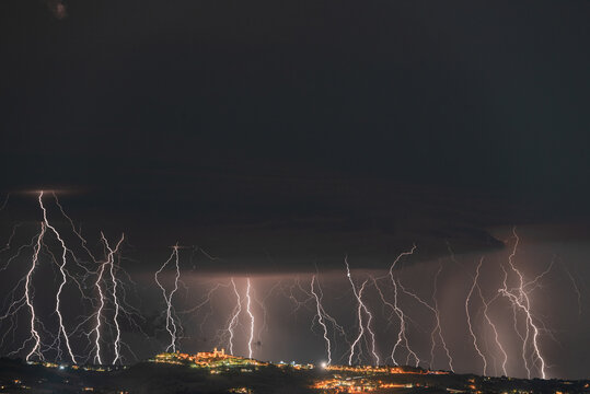 View of multiple lightning strikes illuminating the night sky over the historic town of Montecosaro, Marche, Italy.