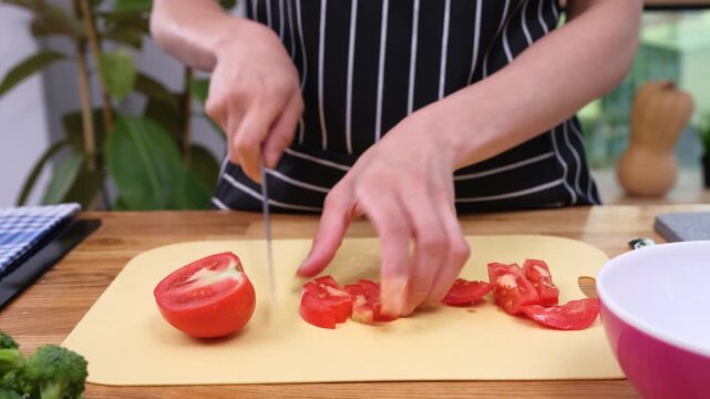 Woman uses sharp knife to cut bright-red tomato into neat pieces. Skilled chef carefully prepares tomato for nutritious homemade salad time lapse