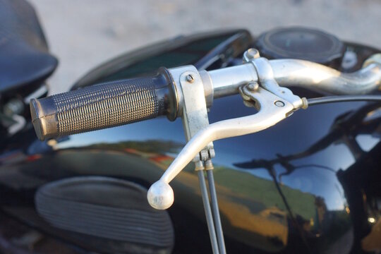 part of a old motorcycle with black gray steering wheel on the summer street