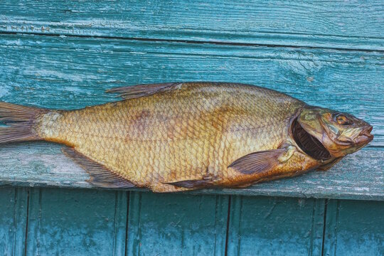 A large brown smoked bream lies on a green wooden table