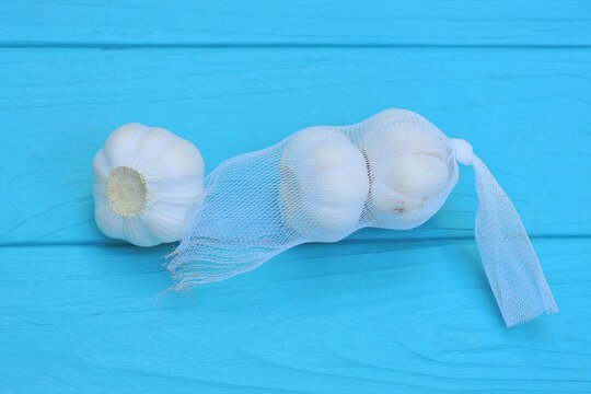 three fresh white heads of garlic in a transparent mesh bag lies on a blue wooden table