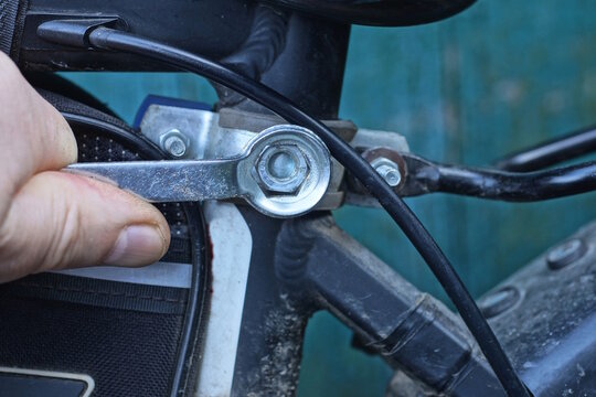 one mans hand with wrench tightening nut on black sports bike on summer street