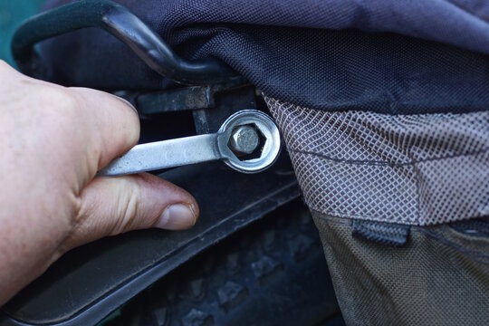 one mans hand with wrench tightening nut on black sports bike on summer street
