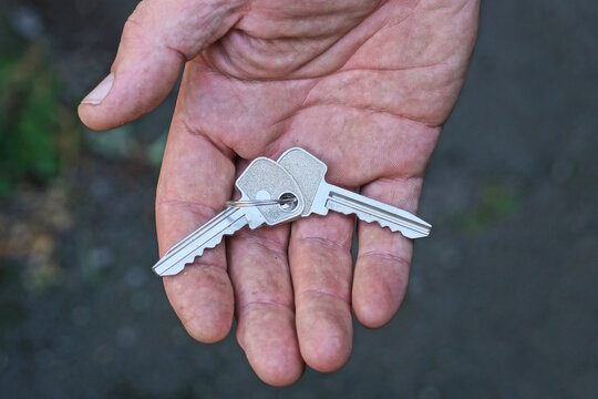 a hand holds a bunch of two old metal gray door keys on the street