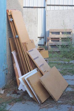 A stack of old brown plywood boards stands against a gray green wall on a street in summer