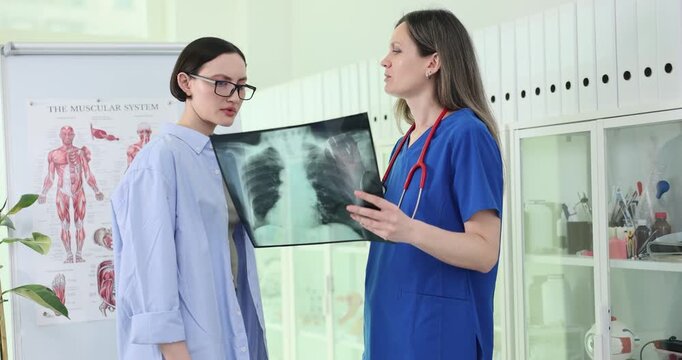 Female doctor reviews chest X-ray with woman during consultation. Physician holds radiograph explaining visible findings during clinic appointment