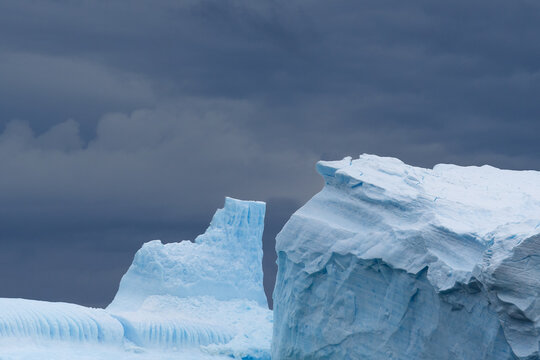 View of icebergs with blue ice formations under a dark cloudy sky in South Orkney Islands.