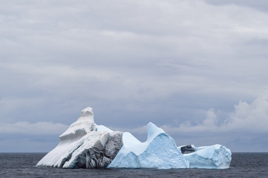 View of a large iceberg floating in the dark ocean under a cloudy sky in the South Orkney Islands.