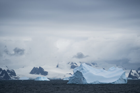 View of icebergs floating in the dark ocean with snow-covered mountains of the South Orkney Islands in the background under a cloudy sky, South Orkney Islands.