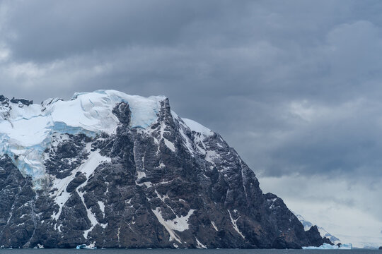 View of the rugged, snow-capped mountain peaks under a dramatic, overcast sky, South Orkney Islands.
