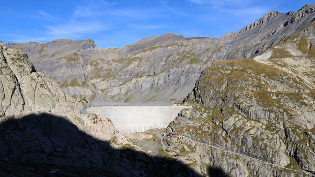 View of the Vieux Emosson Dam nestled within the rugged, rocky peaks of the Swiss Alps under a clear blue sky in Finhaut, Valais, Switzerland.