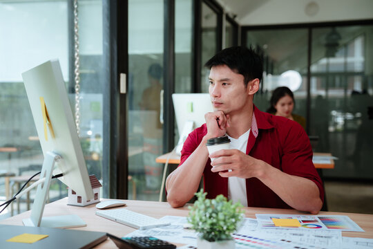 Asian male architect reviewing a residential floor plan on a computer while working on architectural drawings and house design concepts in a modern studio.
