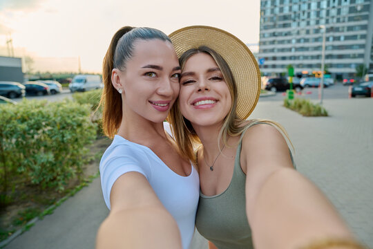 Two smiling young female friends taking selfie on city street summer
