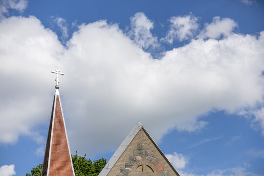 Church roof with Orthodox cross against blue sky and large white clouds in daylight