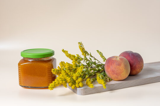 Peach jam in glass jar with fresh peaches and yellow flowers on wooden board with copy space